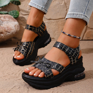 Black textured open-toe wedge sandals with bow detail and adjustable straps.