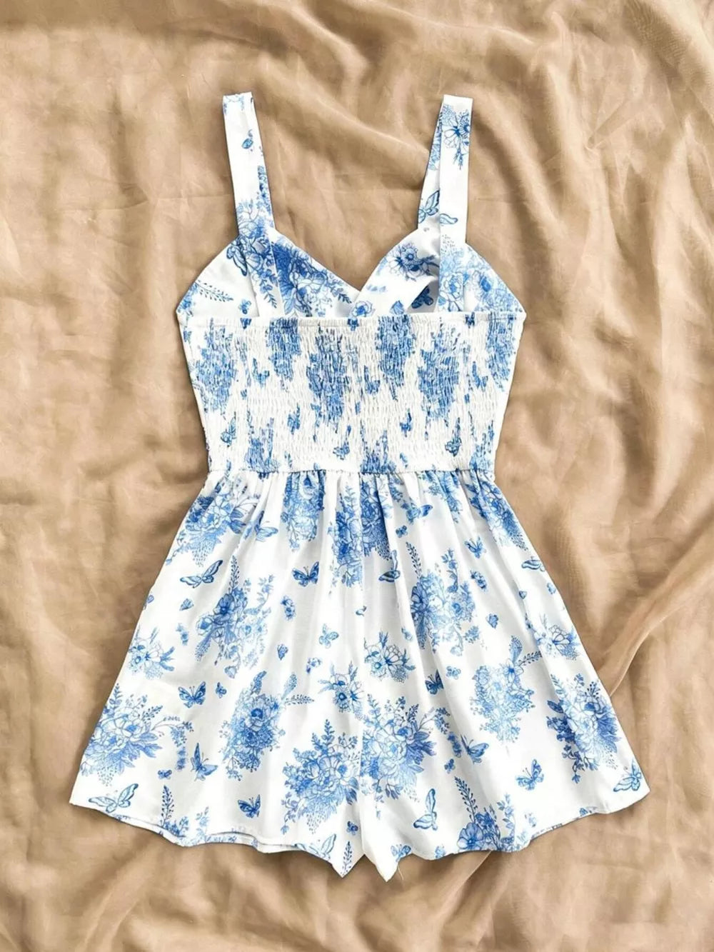 White and blue floral print romper with smocked waist and butterfly details.