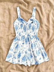 White and blue floral print romper with smocked waist and butterfly details.