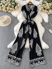 Black wide leg romper with white paisley print, collared, button-down, short sleeves.
