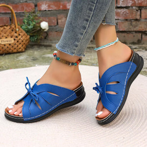 Blue criss-cross wedge sandals with bow detail and white stitching.