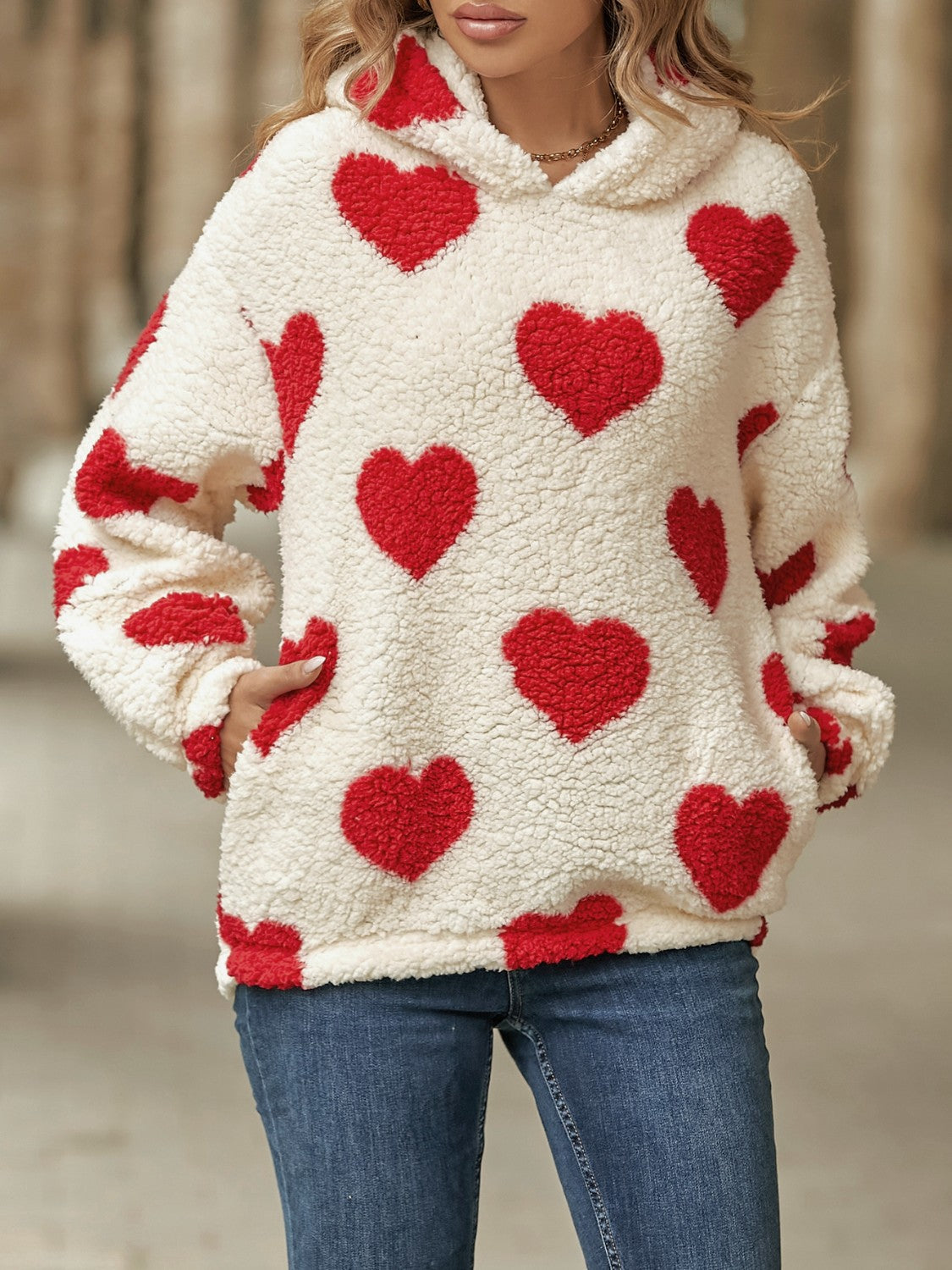 Cream sherpa hoodie with all-over red heart print and front pockets.