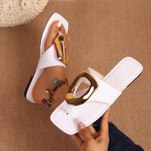 Glossy white toe-post sandals with bold gold buckle detail.
