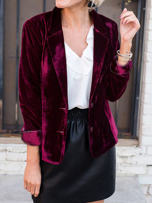 Burgundy velvet blazer with button front and notched lapels, worn over a white ruffled blouse.