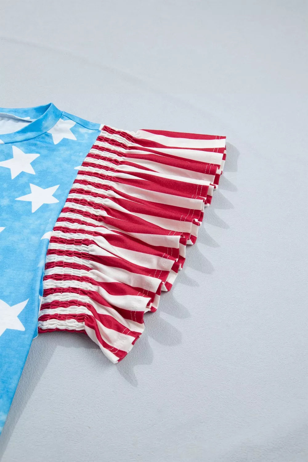 Patriotic t-shirt with blue tie-dye star print and red and white striped ruffle sleeves.