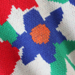 Floral intarsia knit sweater in white with blue, orange, red, and green geometric floral pattern.