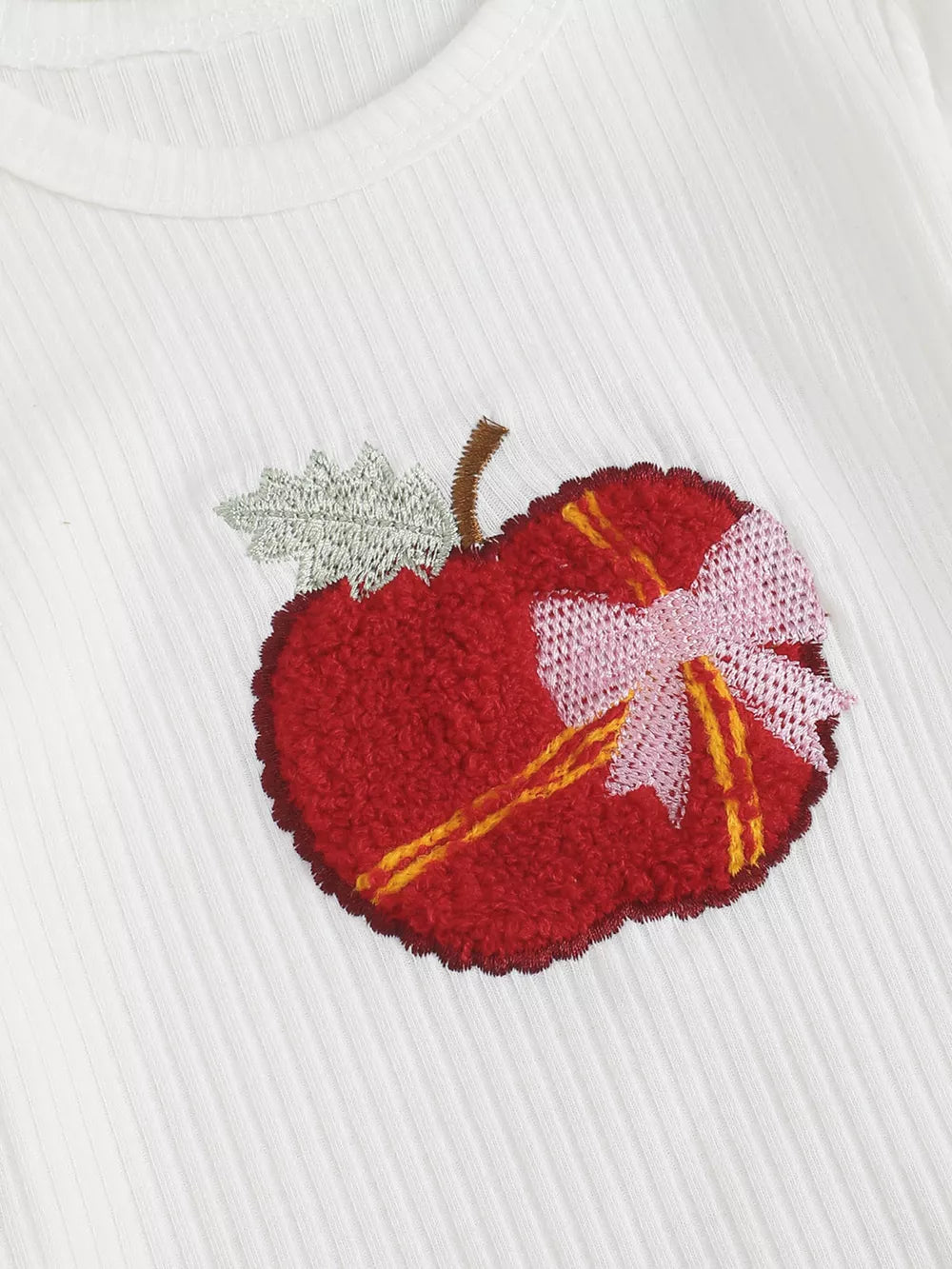 White ribbed cotton bodysuit with a textured red apple applique and pink bow detail.