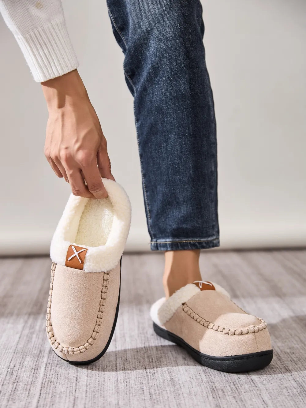 Caramel suede moccasin slippers with shearling lining and decorative stitching.