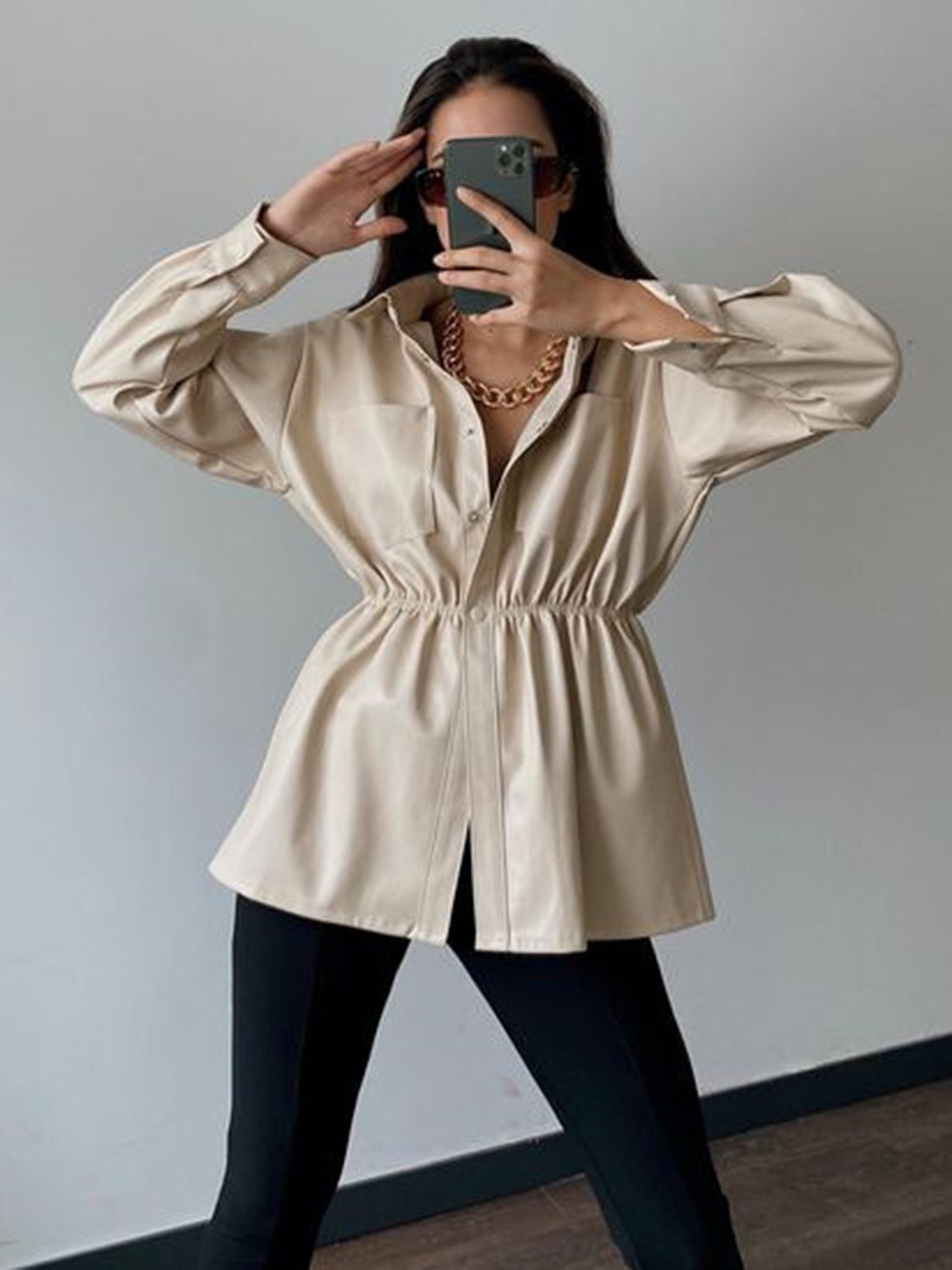 Tan faux leather shirt jacket with gathered waist and button front, styled with a gold chain necklace.