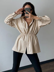 Tan faux leather shirt jacket with gathered waist and button front, styled with a gold chain necklace.