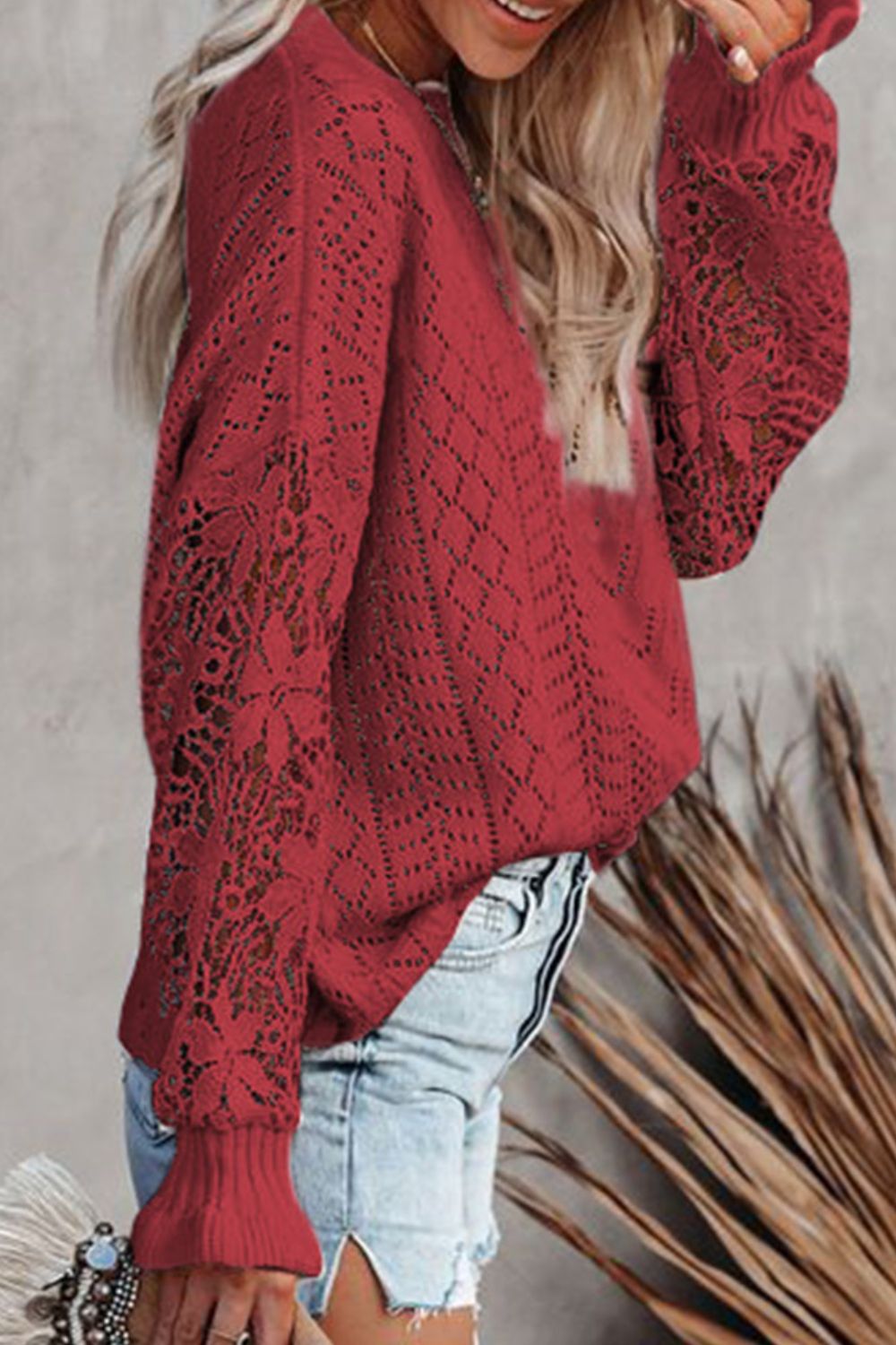 Red openwork knit sweater with lace sleeves and ribbed cuffs, styled with denim shorts.