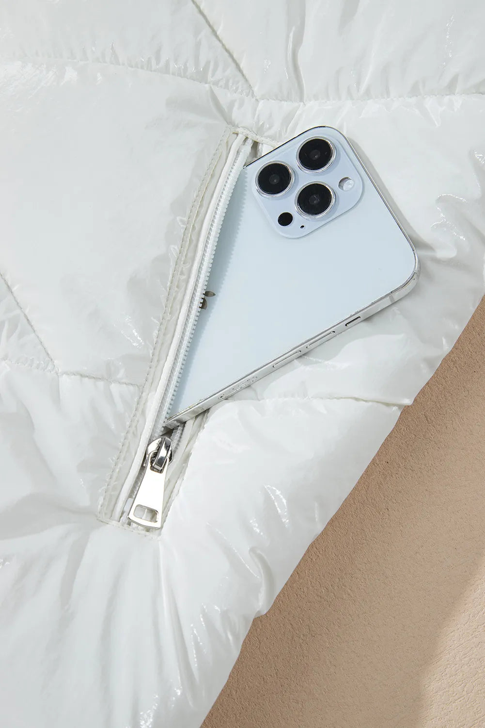 White glossy quilted puffer jacket with a zipper pocket holding a smartphone.