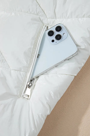 White glossy quilted puffer jacket with a zipper pocket holding a smartphone.