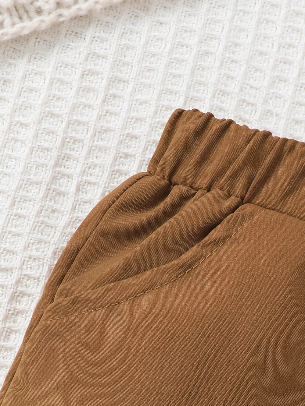 Brown baby pants with elastic waistband and stitched pocket detail.