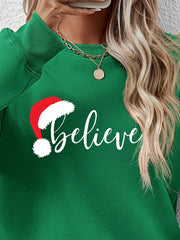 Green raglan sweatshirt with white "believe" text and Santa hat graphic