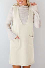Cream sleeveless knit V-neck dress with two front pockets, layered over a ribbed turtleneck.