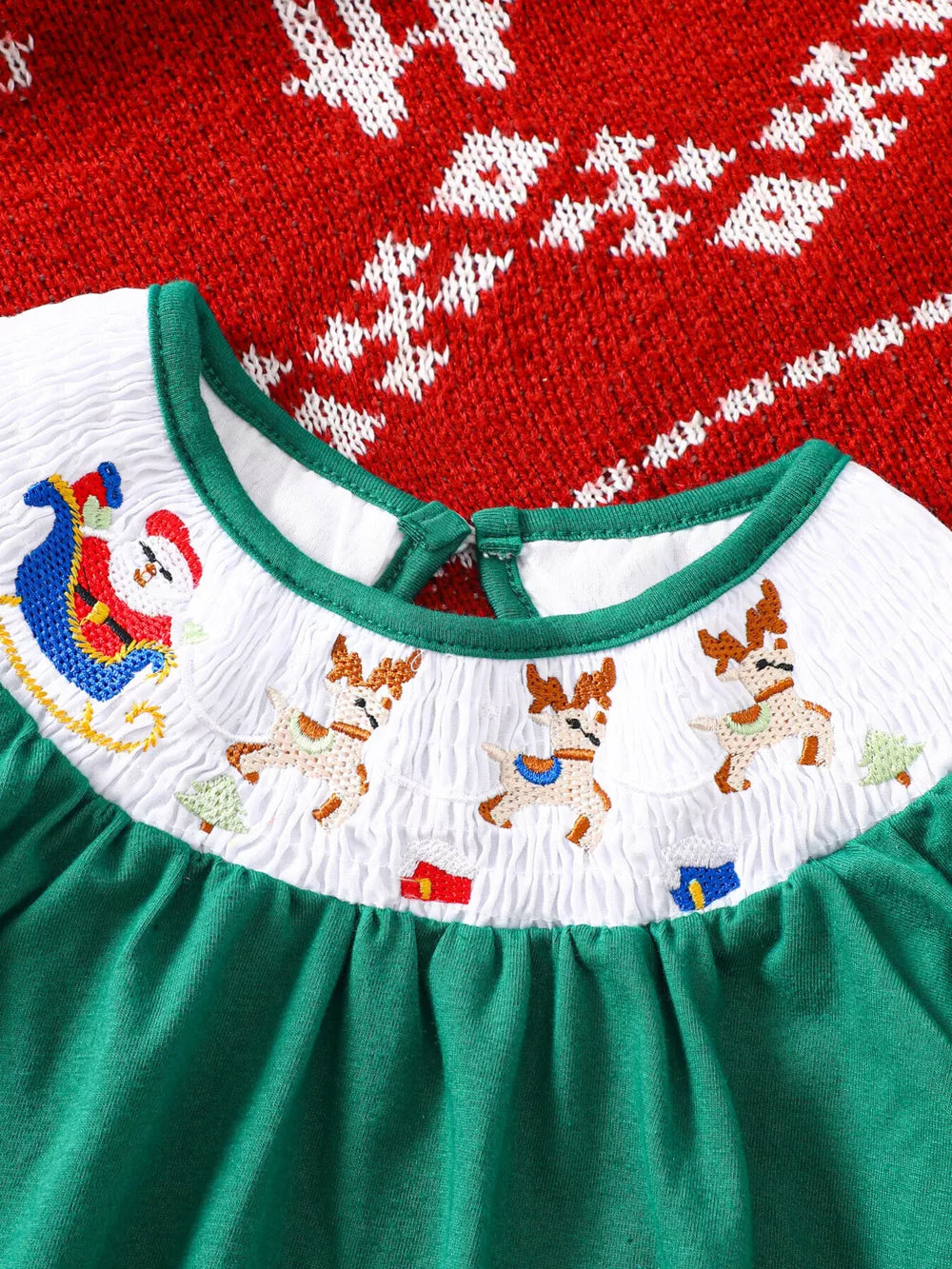 Green A-line baby dress with smocked white yoke featuring embroidered Santa, reindeer, and trees.