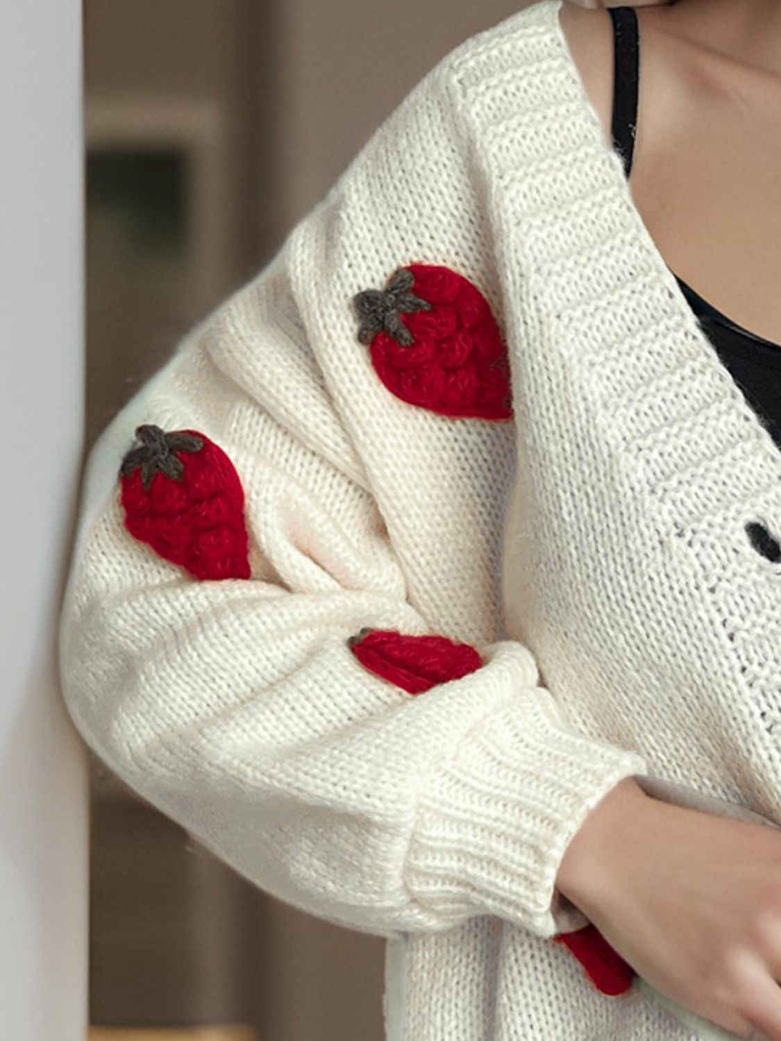 Cream knit cardigan with red strawberry appliqués on the sleeve.