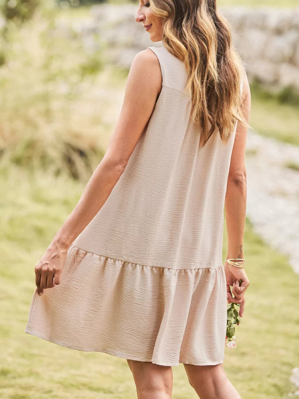 Textured V-neck mini dress with tiered hem and sleeveless design in beige.