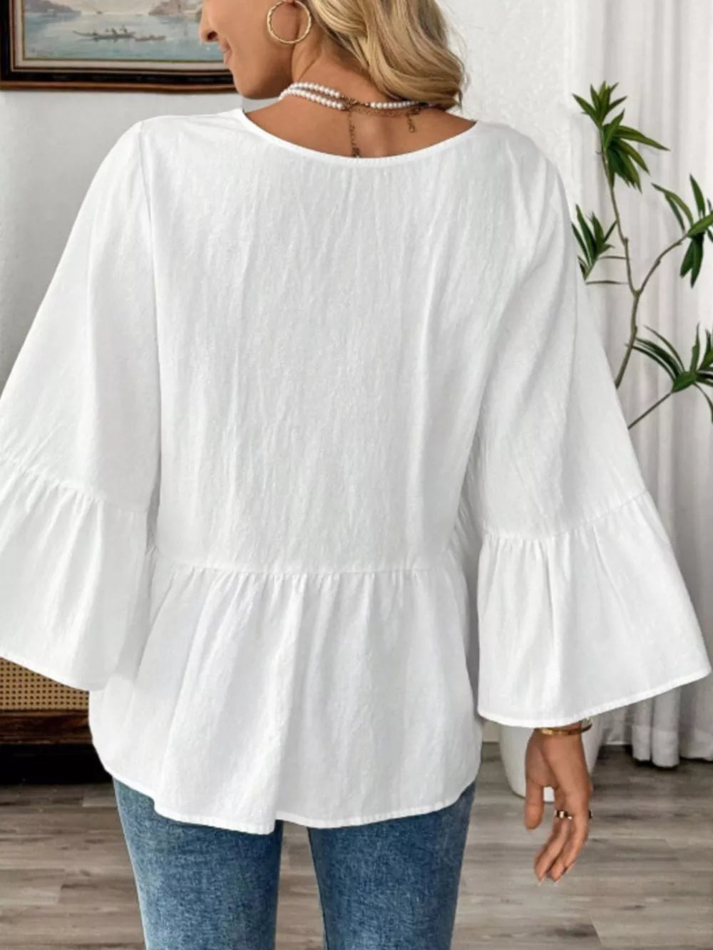 White cotton V-neck blouse with bell sleeves and peplum hem.
