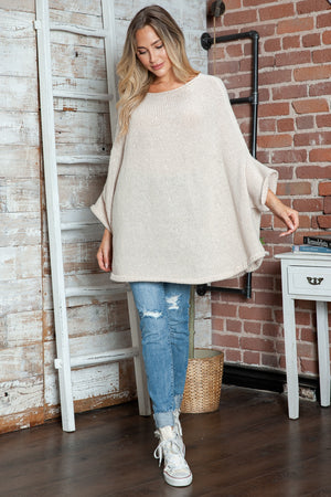Cream knit sweater with cape sleeves and a relaxed fit, styled with distressed jeans.