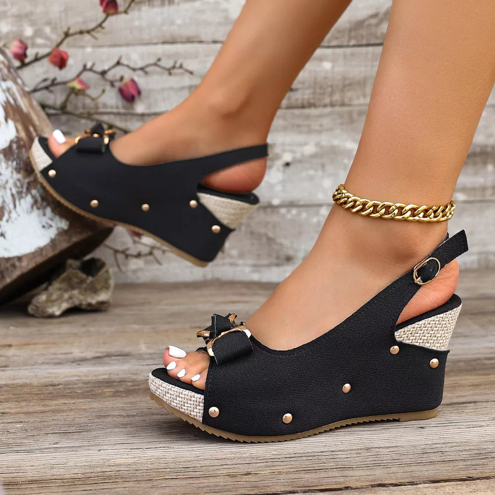 Black peep toe wedge sandals with decorative bow and adjustable strap.