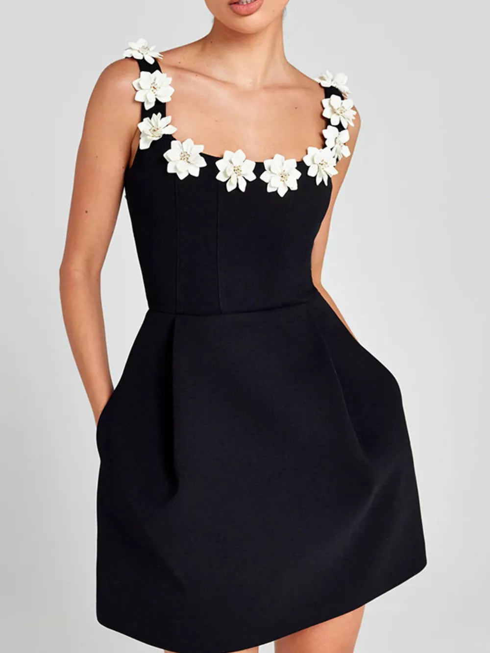 Black mini dress with floral embellishments on straps and neckline, featuring pockets.