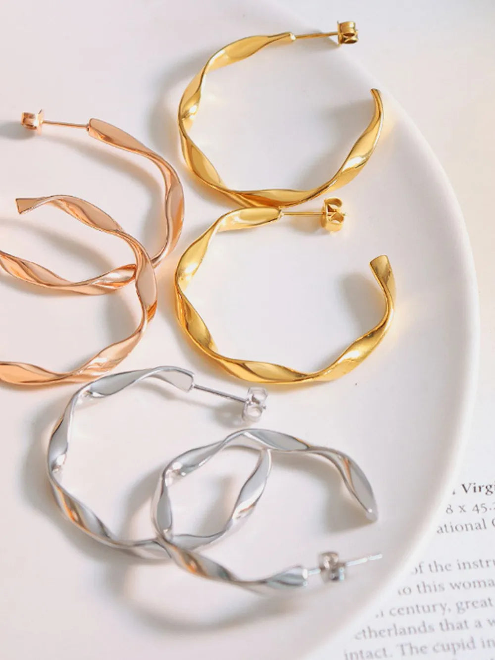 Gold, silver, and rose gold twisted hoop earrings with a sculpted design.