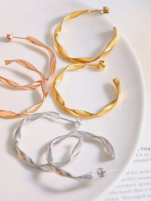 Gold, silver, and rose gold twisted hoop earrings with a sculpted design.