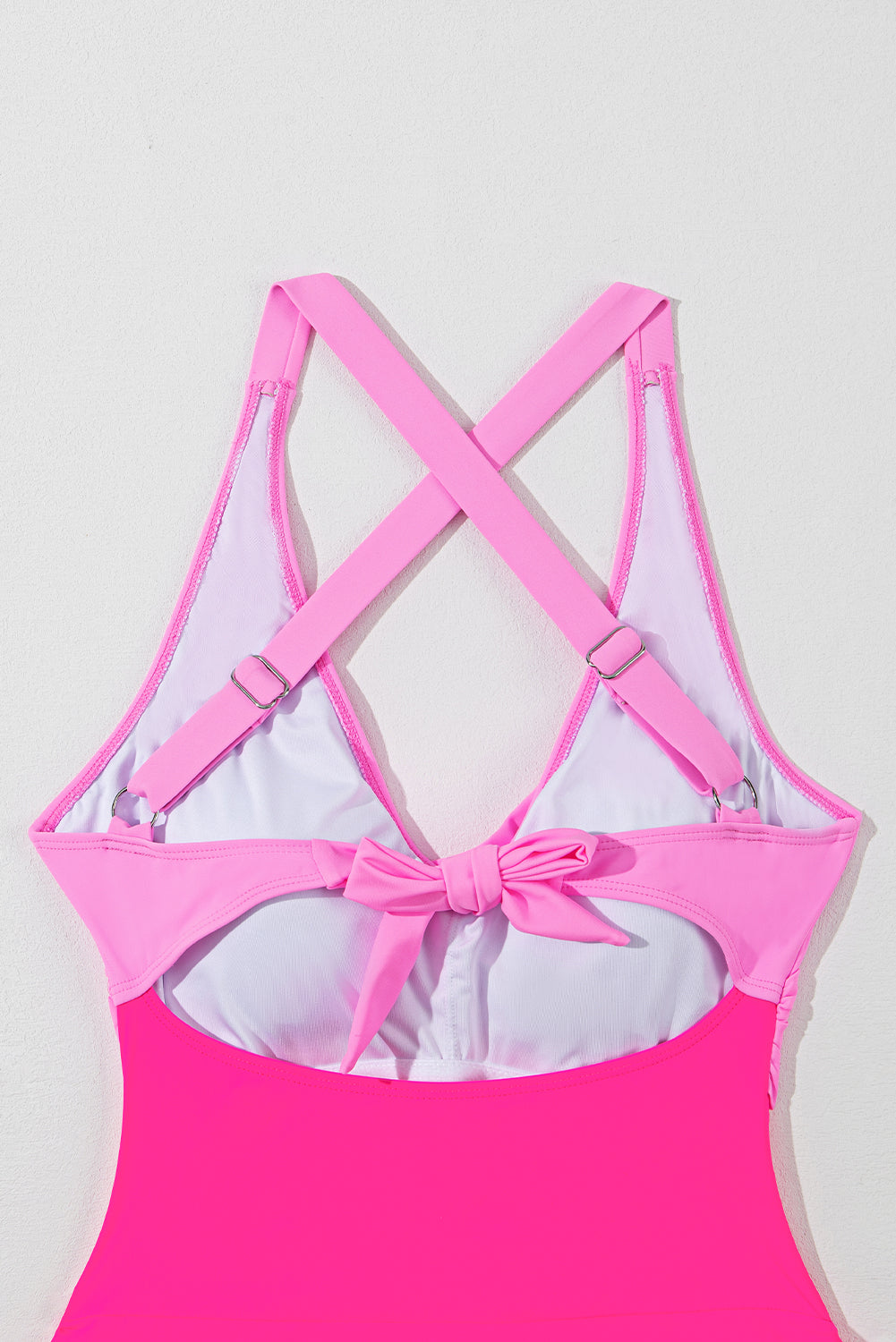 Hot pink one-piece swimsuit with cross-back straps and a bow detail at the back.