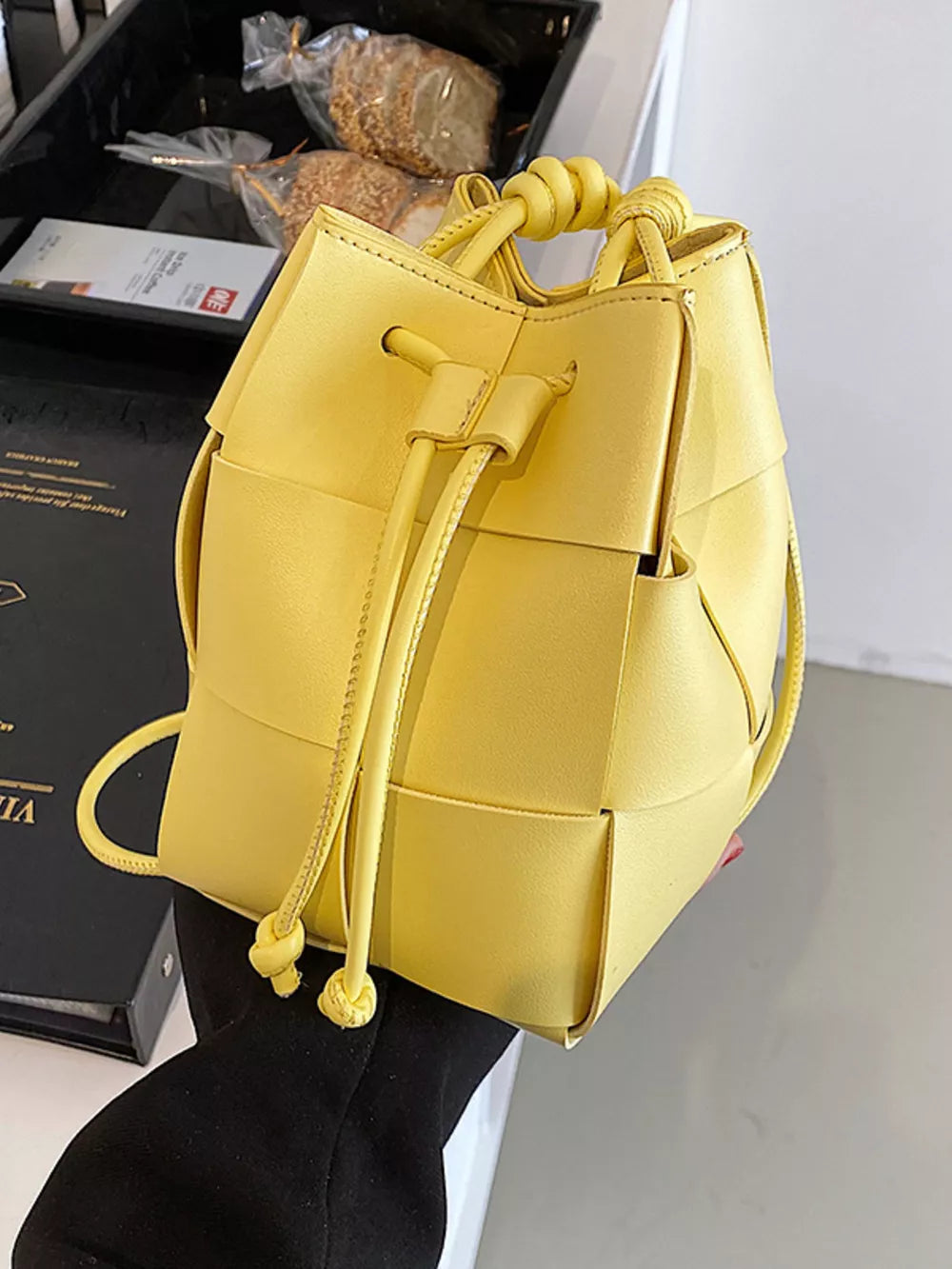 Yellow woven mini bucket bag with drawstring and knotted top handle.