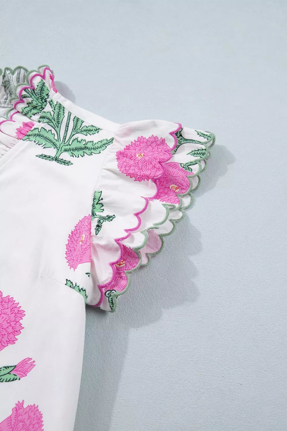 White mini dress with pink floral print, green leaves, and ruffled scalloped trim sleeves.