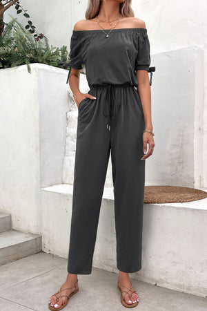 Dark gray off-the-shoulder jumpsuit with tie sleeves, drawstring waist, and pockets.