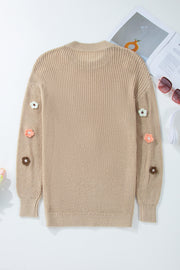 Khaki knit sweater with embroidered floral details on the sleeves.