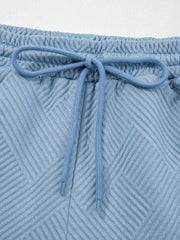 Light blue textured drawstring shorts with elastic waistband and geometric pattern.