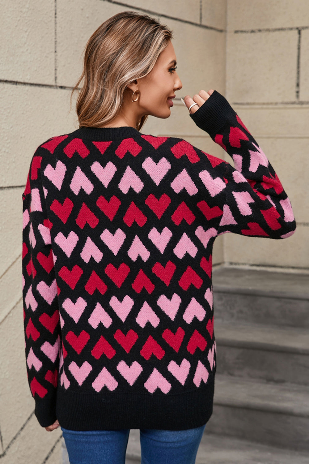 Black knit sweater with allover pink and red heart pattern, crew neck, long sleeves.