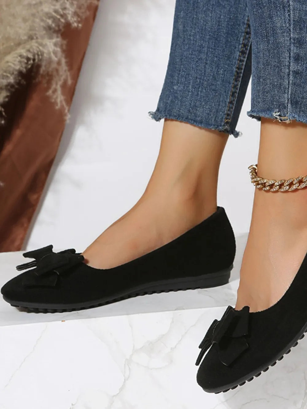 Black suede pointed-toe flats with bow embellishment.