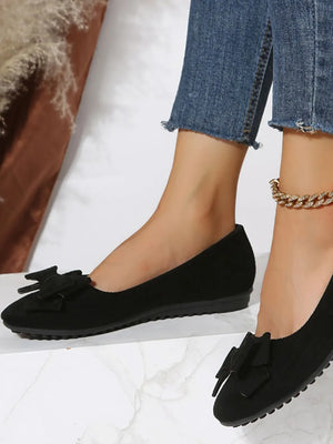 Black suede pointed-toe flats with bow embellishment.