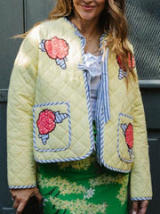 Quilted pastel yellow jacket with floral appliqué and blue trim.