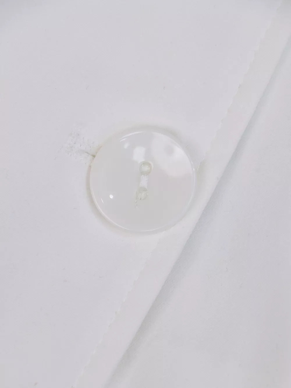 White midi dress with lapel collar, cuffed sleeves, and tie-waist detail, shown with a button closure.