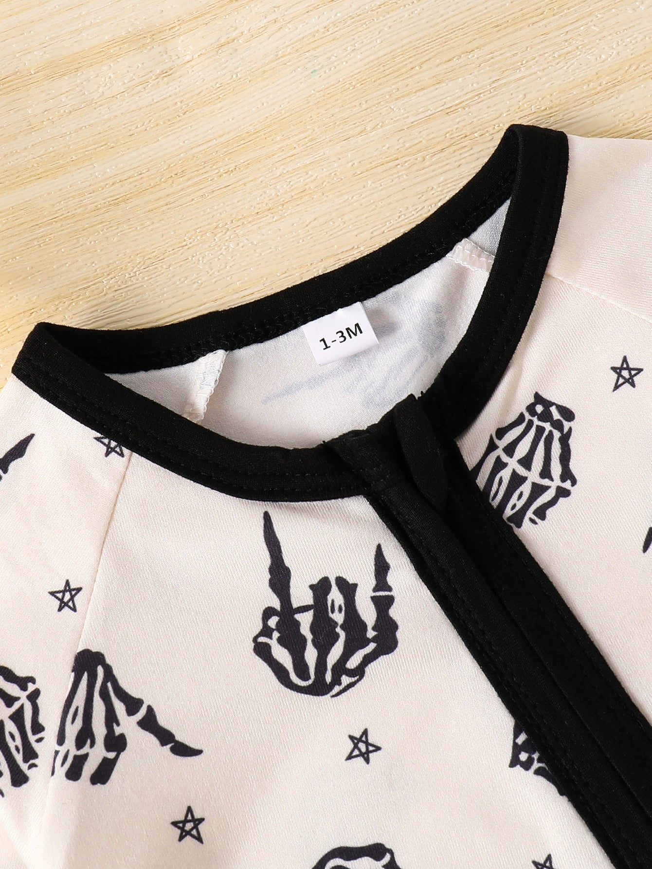 Beige baby one-piece with black skeleton hand print and stars pattern, black trim neckline.