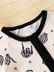 Beige baby one-piece with black skeleton hand print and stars pattern, black trim neckline.