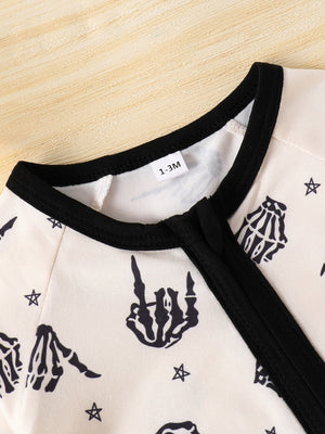 Beige baby one-piece with black skeleton hand print and stars pattern, black trim neckline.