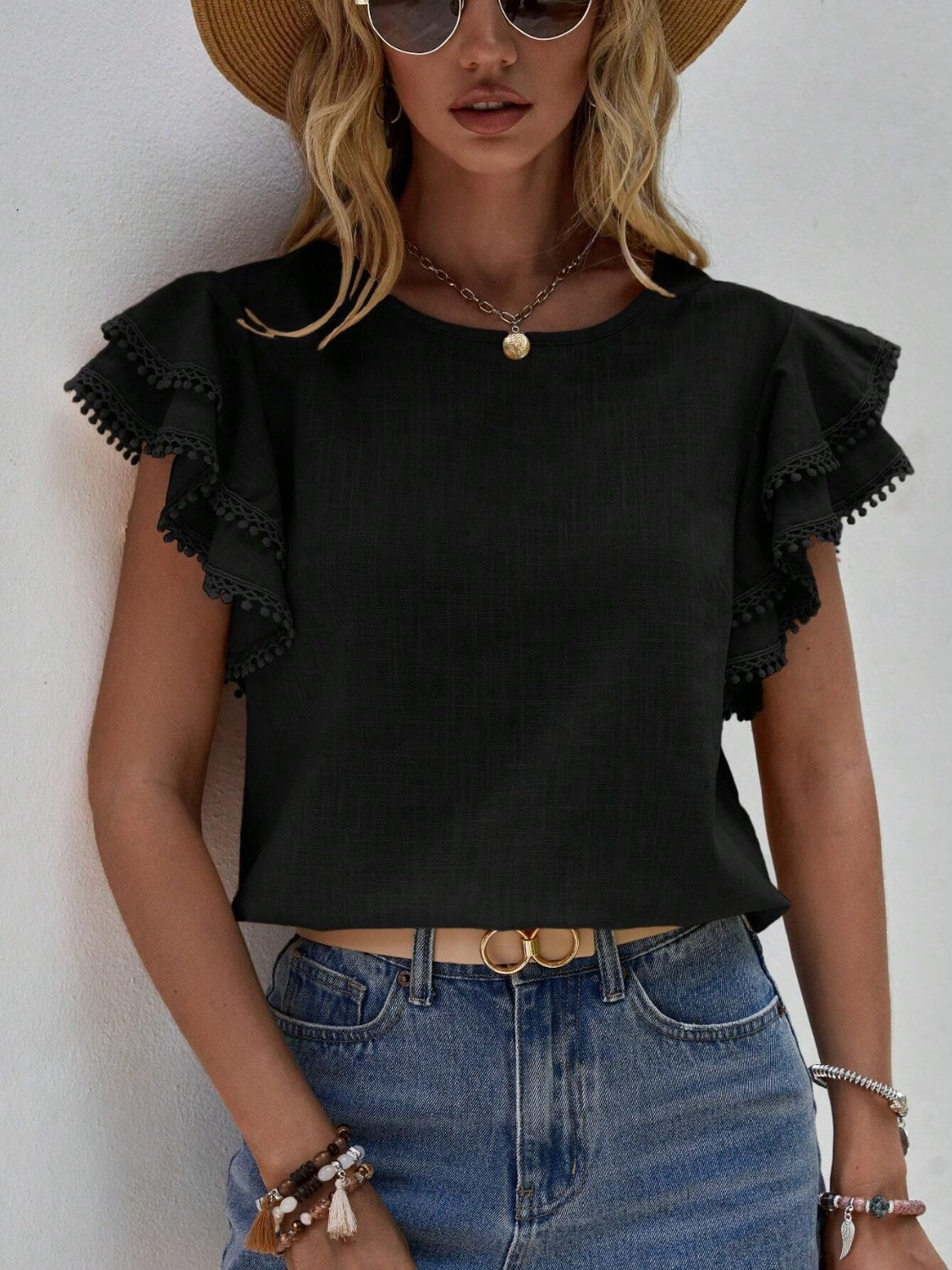Black blouse with pom-pom trimmed ruffle sleeves and a crew neck.