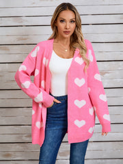Pink acrylic cardigan with white heart intarsia pattern, open front, long sleeves.