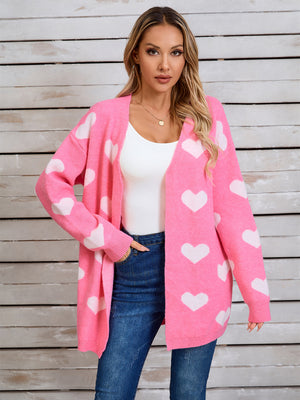 Pink acrylic cardigan with white heart intarsia pattern, open front, long sleeves.