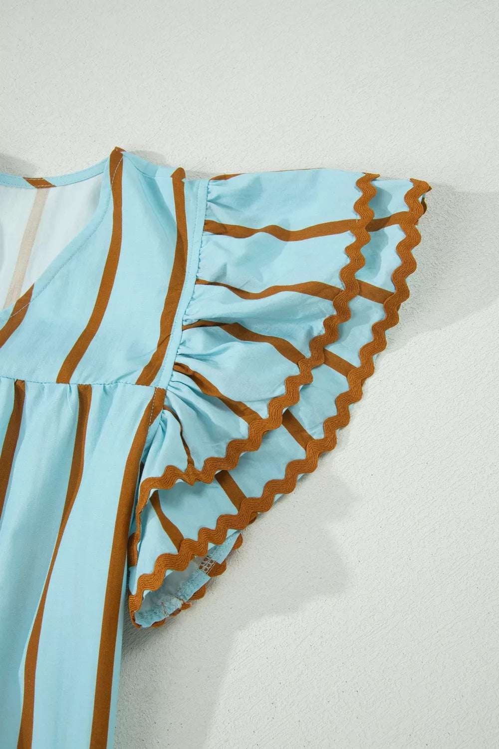 Light blue cotton blend blouse with brown stripes, V-neck, and ruffled sleeves with scalloped trim.
