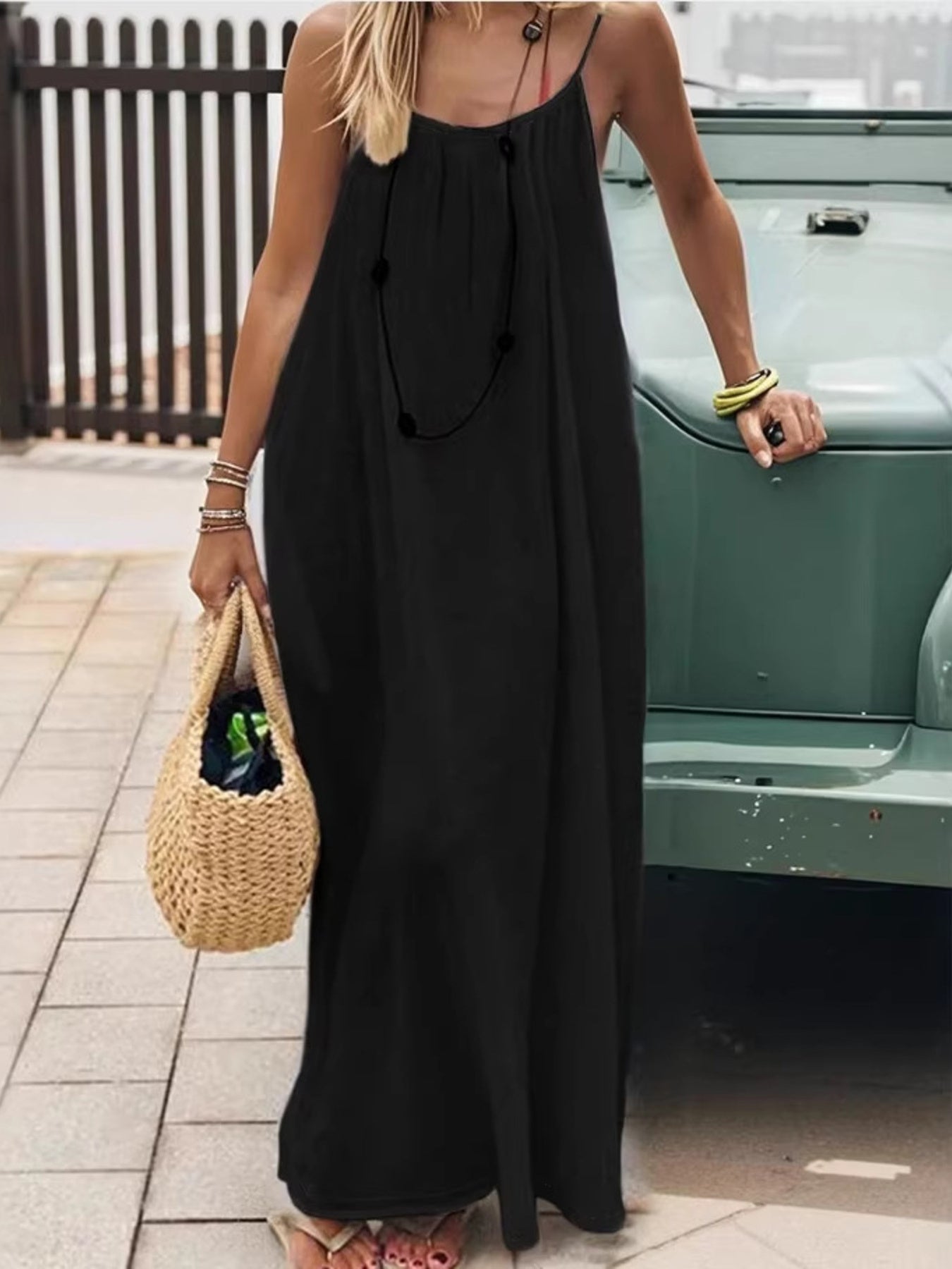 Black backless maxi dress with spaghetti straps and a drawstring waist, styled with a straw bag.