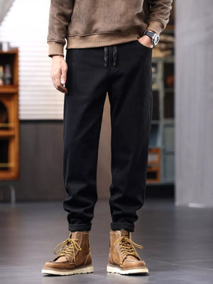 Men's black relaxed fit cotton jeans with drawstring and cuffed ankles.