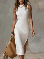 White sleeveless midi dress with high neck and side slit, styled with a straw bag